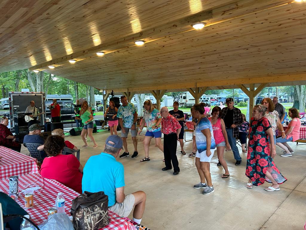 campground visitors line dancing during an event being hosted under a pavilion